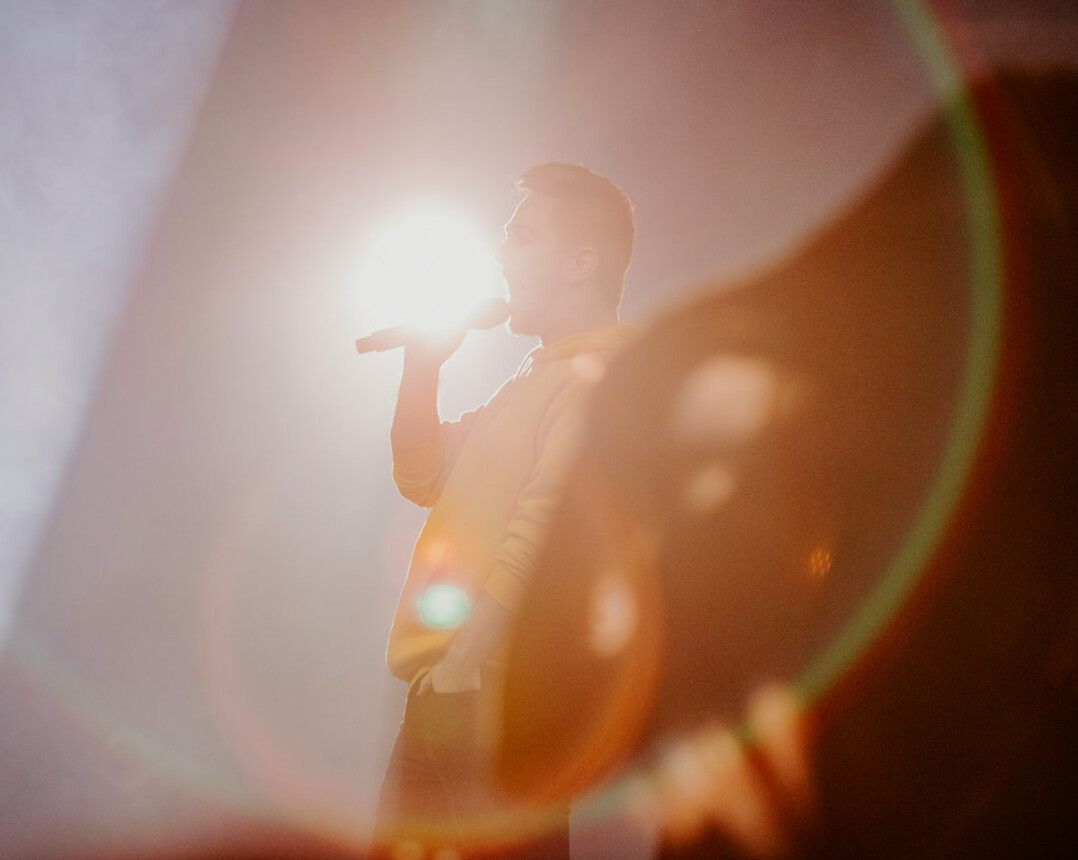 Speaker presenting on stage with a microphone in warm light